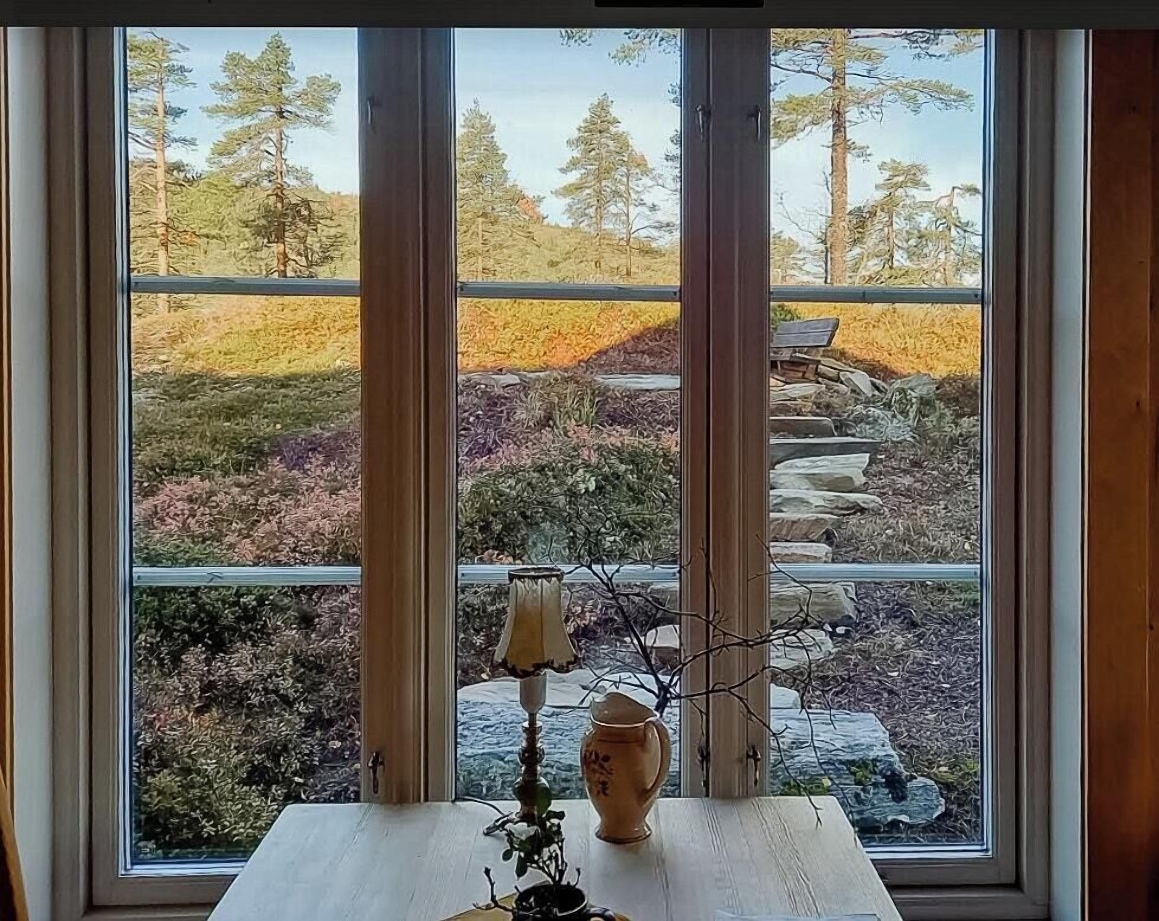 Een kamer met een groot raam dat uitkijkt op een tuin met bomen en een stenen muur.