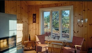 Un interior de madera con un ventanal grande, dos sillones estampados, una mesita y un televisor.