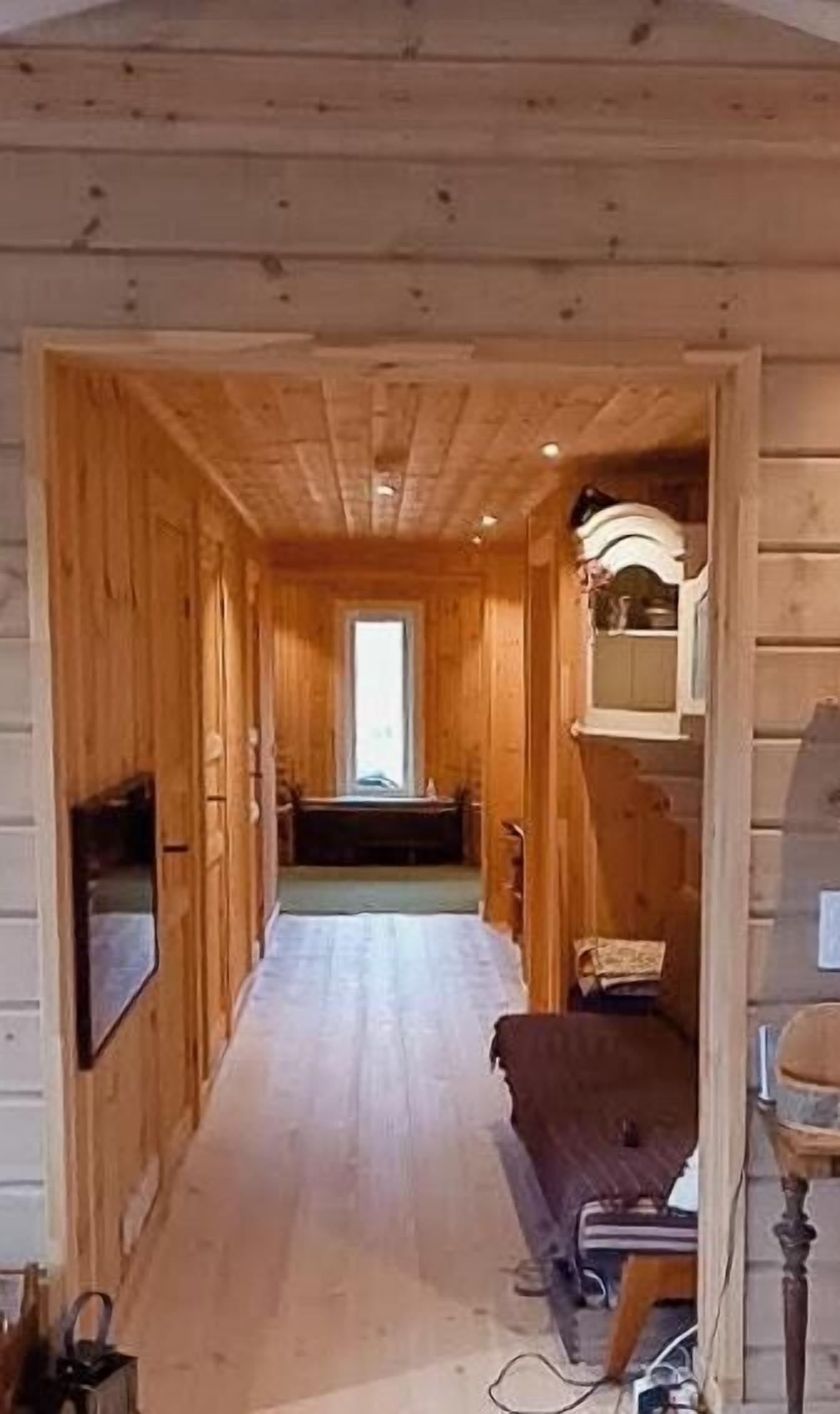 A wooden interior hallway with a television, a bench, and a cabinet.