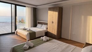 A modern hotel room with two beds, a large wardrobe, and a view of the sea.