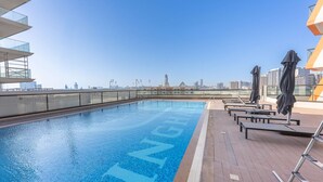 A rooftop swimming pool with a city skyline in the background, surrounded by lounge chairs and umbrellas. - Free Housekeeping Visits During Your Stay - Stayshort - Stylish 1 Bed Apartment in Al Jaddaf for 2 With Pool Gym (Dubai)