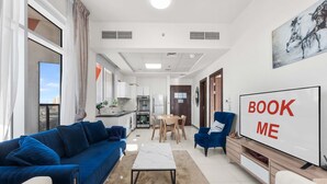 A modern living room with a sofa, coffee table, TV, and a dining area with chairs and a table. - Free Housekeeping Visits During Your Stay - Stayshort - Stylish 1 Bed Apartment in Al Jaddaf for 2 With Pool Gym (Dubai)