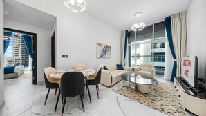 A modern living room with a dining area, a sofa, a TV, and a large window with curtains. - Free Housekeeping Visits During Your Stay - Stayshort - Stunning 2BR in Arjan That Sleeps 4 (Dubai)