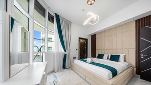 A modern hotel room with a large bed, a vanity with a mirror, a window with curtains, and a ceiling light fixture. - Free Housekeeping Visits During Your Stay - Stayshort - Stunning 2BR in Arjan That Sleeps 4 (Dubai)