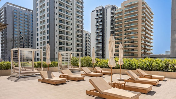 A rooftop lounge area with sun loungers and umbrellas, surrounded by high-rise buildings. - Free Housekeeping Visits During Your Stay - Stayshort - 1BR in Jumeirah Village Circle Sleeps 4 With Balcony (Dubai)