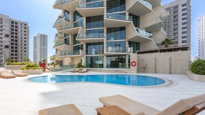 A modern building with a swimming pool, lounge chairs, and a view of surrounding high-rise buildings. - Free Housekeeping Visits During Your Stay - Stayshort - 1BR in Jumeirah Village Circle Sleeps 4 With Balcony (Dubai)