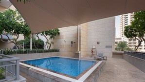 A rectangular indoor pool with a tiled edge, surrounded by a low stone wall, under a canopy, with a chair and a fire extinguisher nearby. - Free Housekeeping Visits During Your Stay - Stayshort - Modern Studio That Sleeps 4 in Downtown (Dubai)