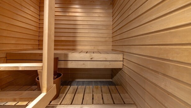 Eine Sauna mit Holzwänden und -bänken, eine Bank im Vordergrund und ein kleiner Mülleimer.