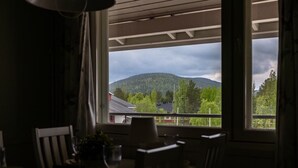 Ein Zimmer mit großem Fenster, einem Sessel, einem Tisch und einer Pendelleuchte.
