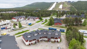 A commercial building with multiple units, a parking lot, and a road with vehicles. - Levistar 912 | 2BR | Sauna | Steps to Shops & Ski (Kittilä)