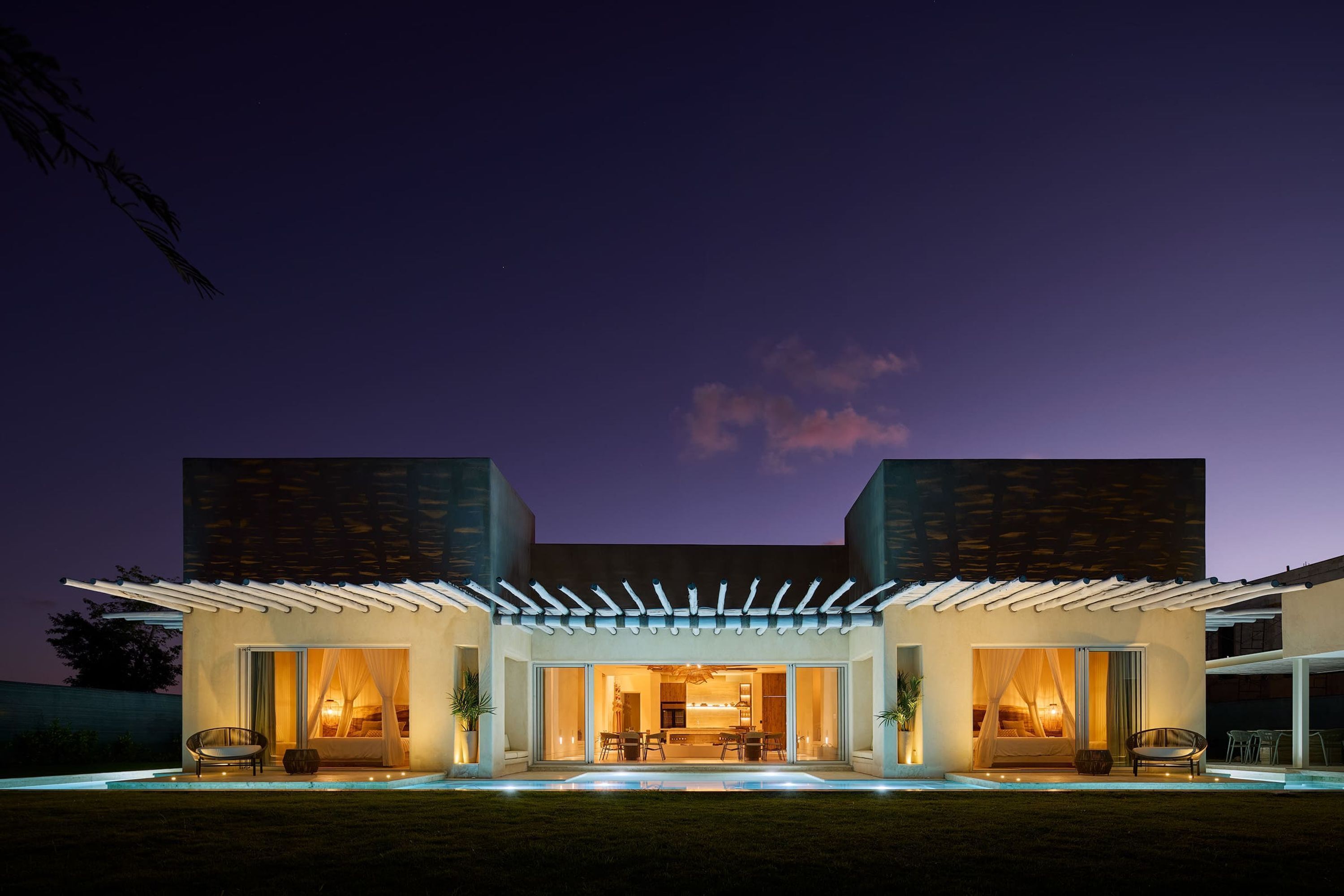 A modern house with a covered patio, large sliding glass doors, and a well-lit interior.