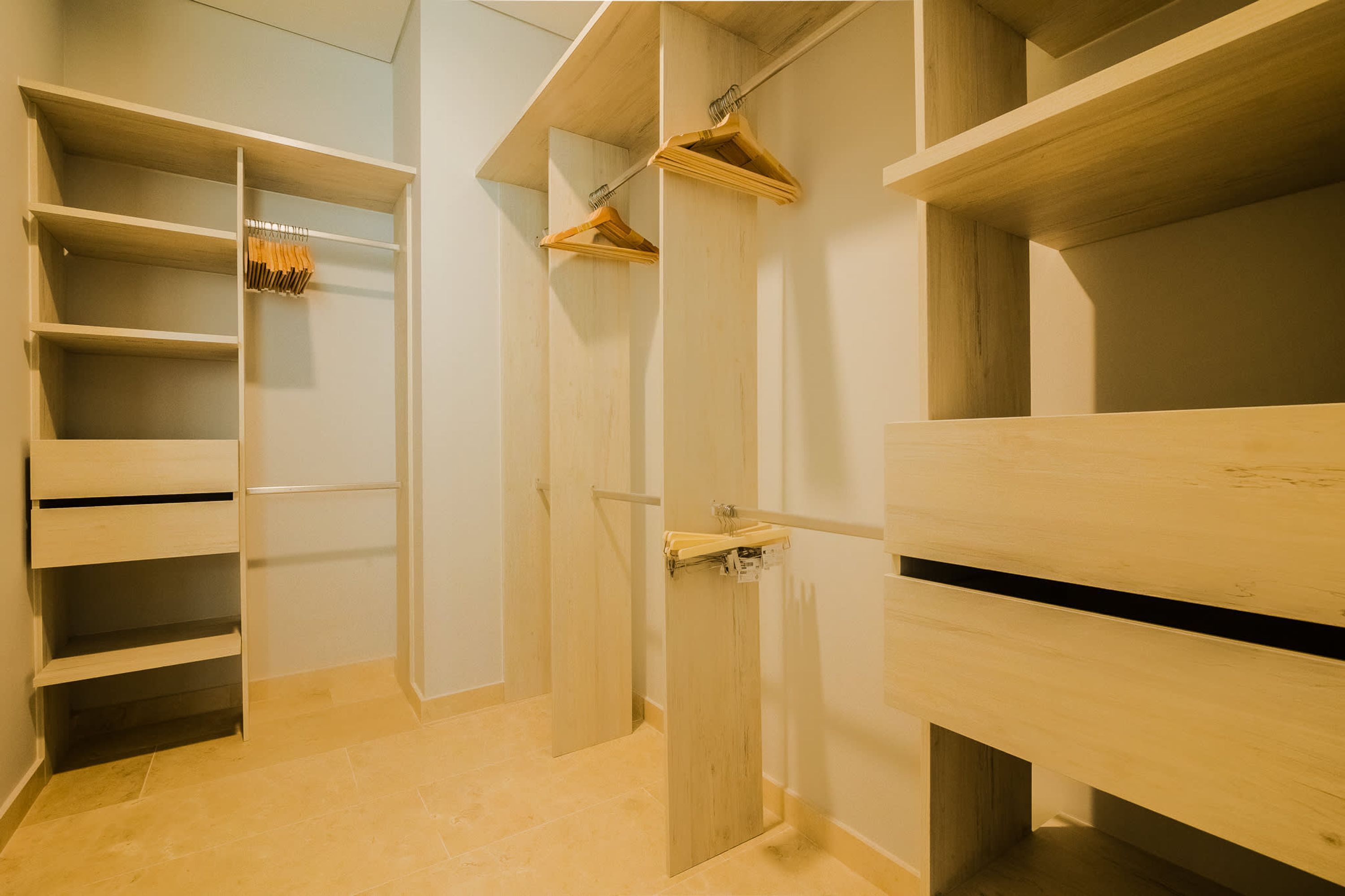 A walk-in closet with open doors, wooden shelves, and hanging space.