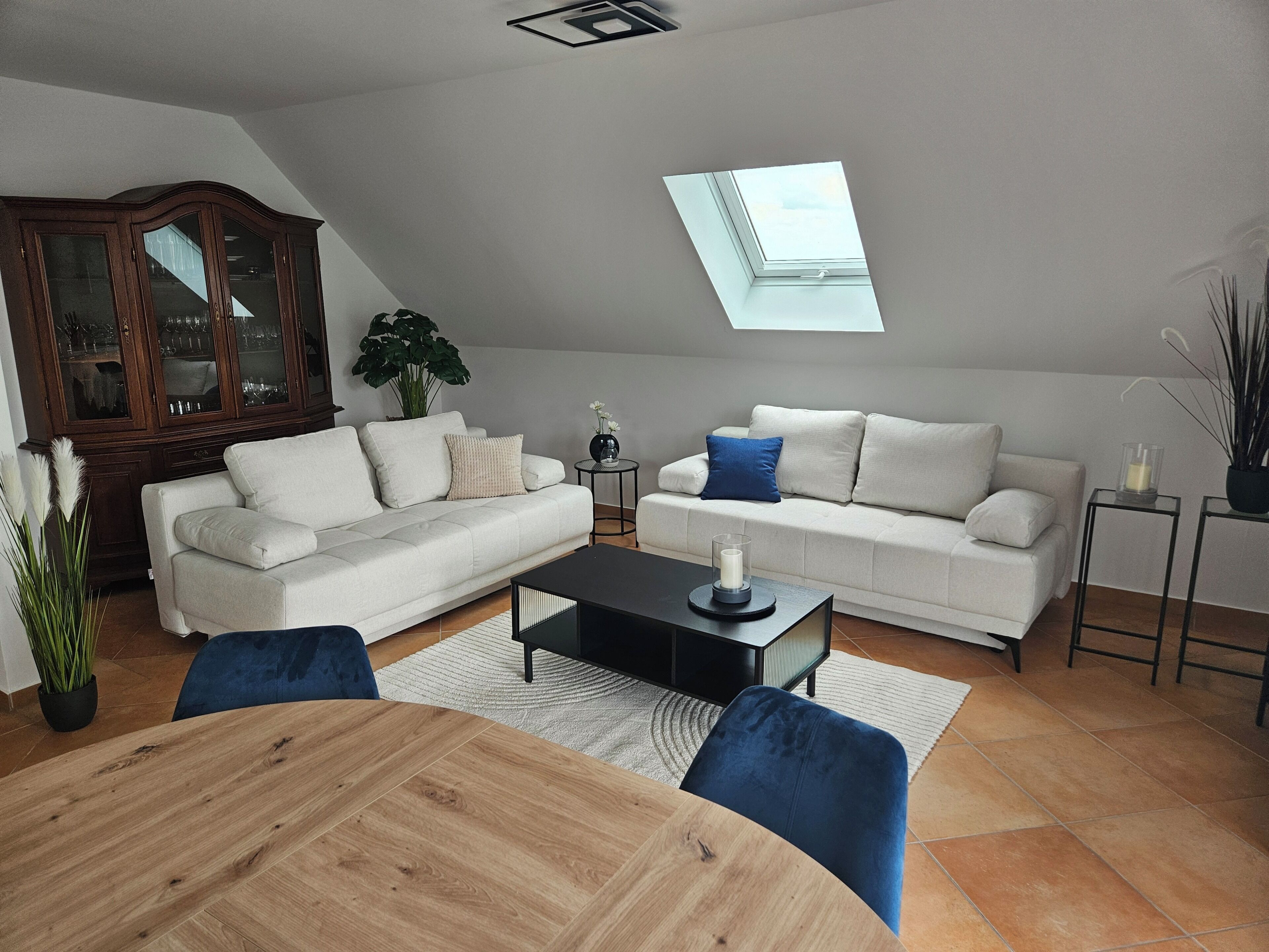 Ein modernes Wohnzimmer mit einem Holzesstisch, zwei weißen Sofas, einem Glastisch und einem Oberlicht.