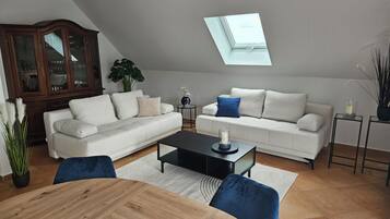 Ein modernes Wohnzimmer mit einem Holzesstisch, zwei weißen Sofas, einem Glastisch und einem Oberlicht.