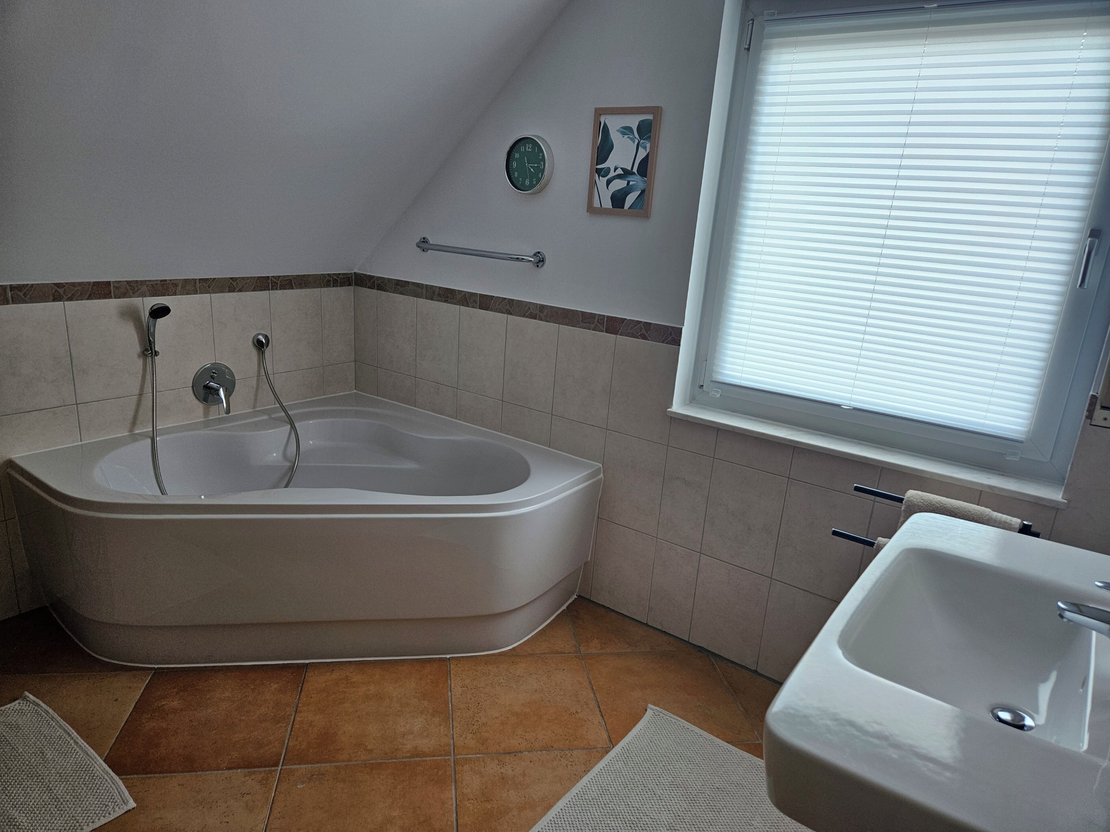 A bathroom with a bathtub, a sink, a window with blinds, a clock, and a towel rack.