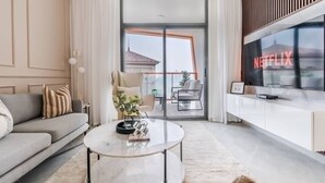 Una sala de estar moderna con un sofá, una mesa de centro, un televisor y un gran ventanal corredizo que da a un balcón.