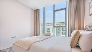 Ein Hotelzimmer mit großem Fenster, einem Bett mit beiger Decke, einer Couch mit gemusterten Kissen und Blick auf Gebäude.