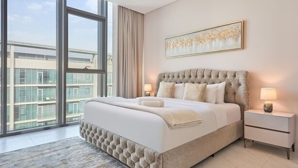 Ein geräumiges Schlafzimmer mit einem großen Bett, zwei Nachttischen, einem Fenster mit Blick auf die Stadt und einem gerahmten Kunstwerk an der Wand.