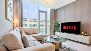 Ein modernes Wohnzimmer mit einer Couch, einem Couchtisch, einem Fernseher mit dem Schriftzug 'NETFLIX' und einem großen Fenster.