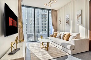 Ein modernes Wohnzimmer mit großem Flachbildfernseher, einer Couch, einem Couchtisch und Blick auf hohe Gebäude.