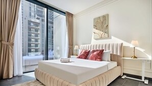 A modern hotel room with a large bed, a view of a cityscape, a bedside table with a lamp, and a wall-mounted artwork. - The Crest C Luxury Retreat Stylish Serene (Dubai)