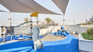 A playground with slides and climbing structures, surrounded by blue flooring and shaded by large canopies. - The Crest C Luxury Retreat Stylish Serene (Dubai)