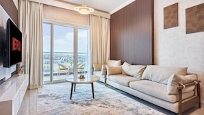 A modern living room with a sofa, a coffee table, a TV, and a large window with curtains. - 2 Bedroom Apartment Close to Miracle Tower (Dubai)