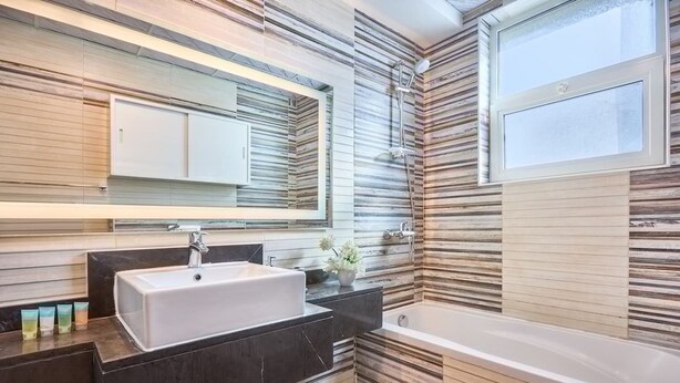 A modern bathroom with a large mirror, a sink, a bathtub, and a window. - 2 Bedroom Apartment Close to Miracle Tower (Dubai)