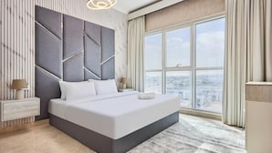 A modern bedroom with a large bed, a city view, and a unique geometric headboard. - 2 Bedroom Apartment Close to Miracle Tower (Dubai)
