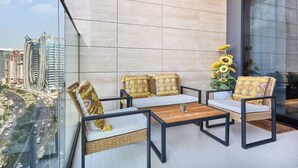 A balcony with a view of a cityscape, furnished with wicker chairs and a wooden table. - Luxury Studio in Trillionaire Residence (Dubai)