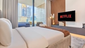 A modern hotel room with a large bed, a TV mounted on the wall, a view of the cityscape, and a wooden panel accent. - Luxury Studio in Trillionaire Residence (Dubai)