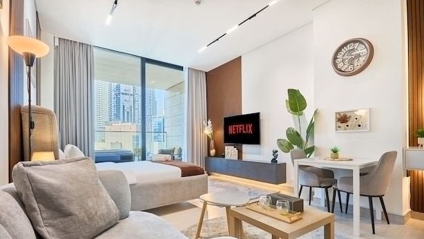 A modern living room with a sofa, coffee table, TV, and a dining area with chairs and a table. - Luxury Studio in Trillionaire Residence (Dubai)
