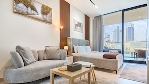 A modern hotel room with a sofa, a bed, a small table, and a large window with a city view. - Luxury Studio in Trillionaire Residence (Dubai)