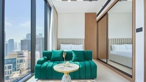 Et moderne hotelværelse med et stort vindue, en grøn sofa, et rundt sofabord og en seng med hvide sengetøj.