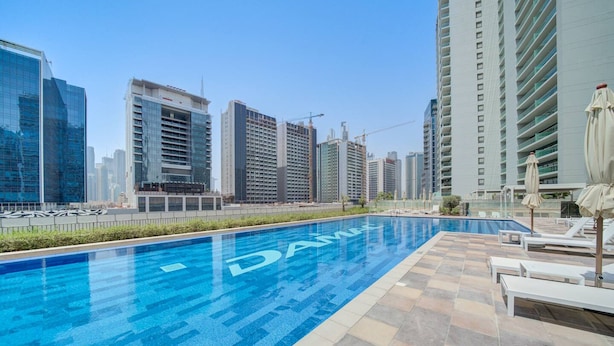 A swimming pool with 'DAM' written on the water, surrounded by lounge chairs and umbrellas, with high-rise buildings in the background. - Classic Arabian Elegance With City Views (Dubai)