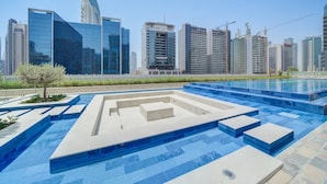 A modern swimming pool with geometric patterns, surrounded by high-rise buildings and construction cranes. - Classic Arabian Elegance With City Views (Dubai)