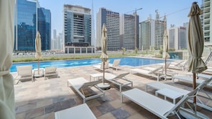 A rooftop pool area with lounge chairs and umbrellas, overlooking a cityscape with modern buildings. - Classic Arabian Elegance With City Views (Dubai)