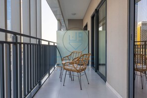A balcony with wicker chairs, a glass wall, and a logo. - Cozy One Bedroom Apartment in Zada Tower (Dubai)