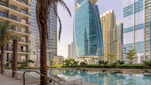 A modern hotel with a pool area, palm trees, and high-rise buildings in the background. - 1BR Zada Tower l Two Balconies City Views (Dubai)
