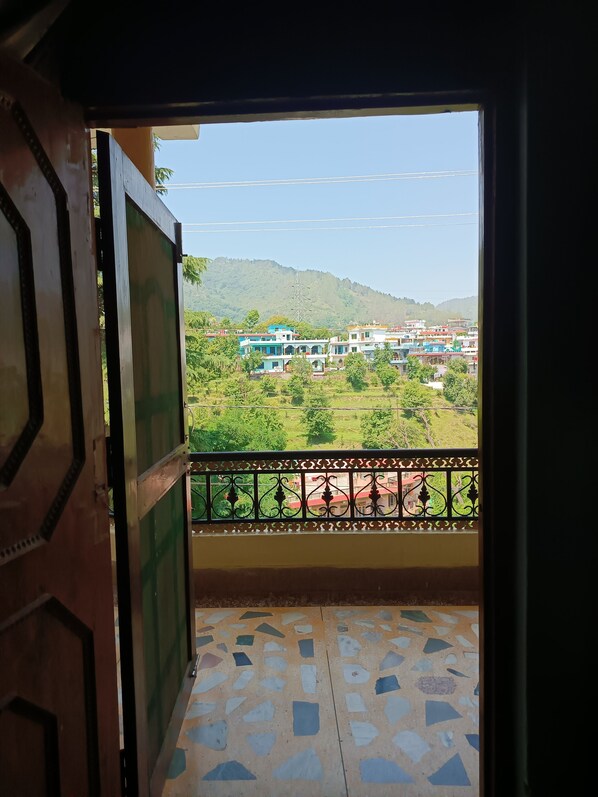 A balcony with a patterned floor, a view of a green landscape, and a building with colorful facades.