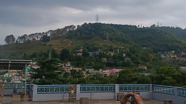 Eine hügelige Landschaft mit Wohngebäuden, einem blauen Geländer und einem Strommasten.