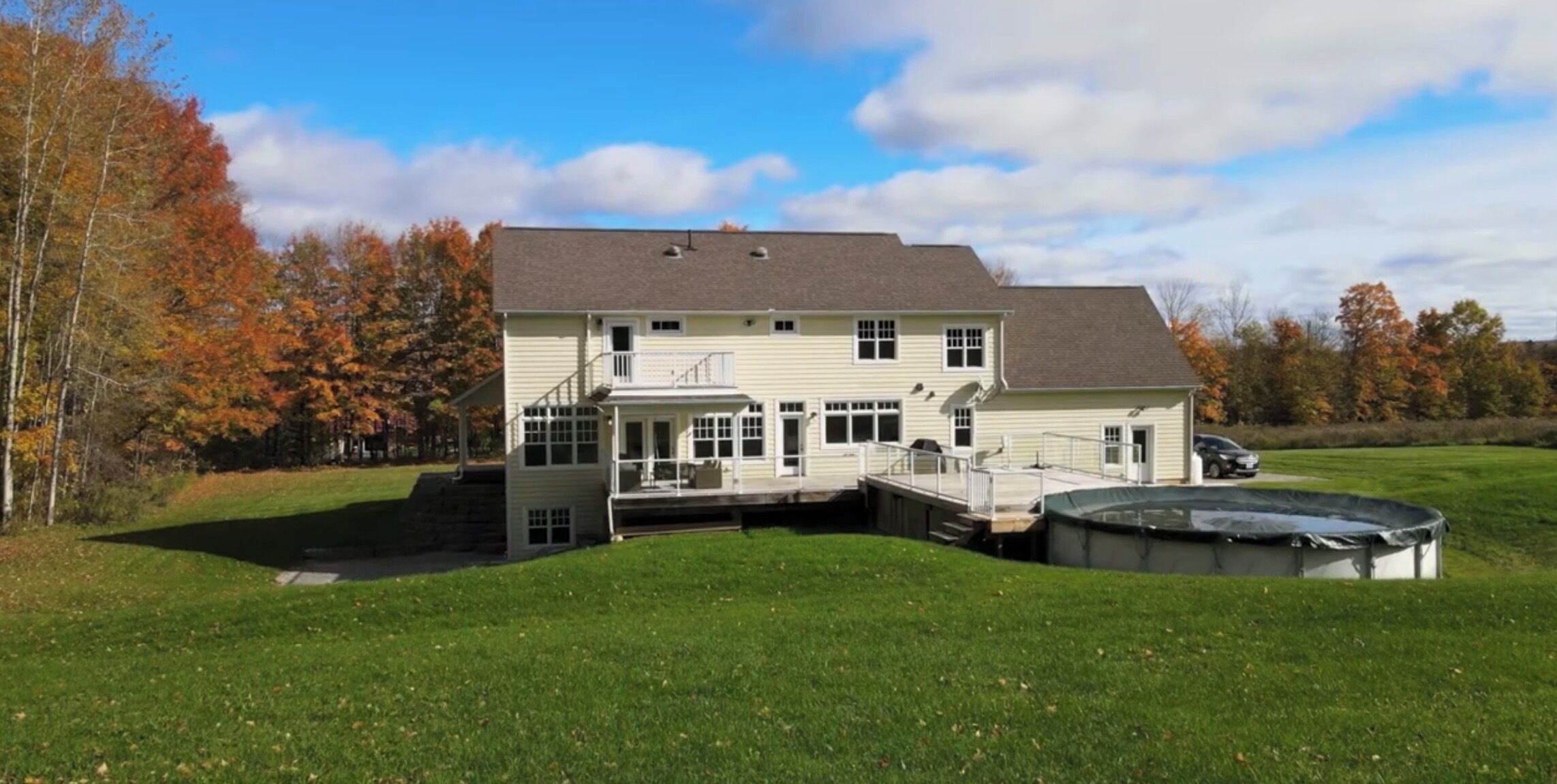 A two-story house with a covered patio, a swimming pool, and a large lawn.
