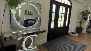 Un couloir avec un grand miroir, une porte noire, un paillasson gris et une plante en pot.