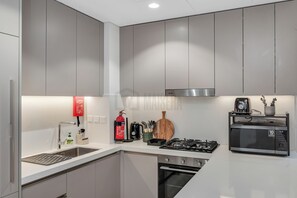 A modern kitchen with grey cabinets, a stainless steel range hood, a gas stove, a microwave, and a fire extinguisher. - Stylish 2BR Riviera - Pool & Gym - Canal Walk (Dubai)