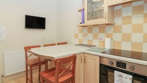 A kitchen with a dining table, chairs, a TV, a stove, and a tiled backsplash. - Pincerna Apartment Suite 1a (Aberdeen)