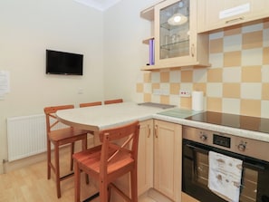 A kitchen with a dining table, chairs, a TV, a stove, and a tiled backsplash. - Pincerna Apartment Suite 1a (Aberdeen)