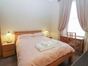 A neatly made bed with pillows, two bedside lamps, a wooden chair, and a desk with a chair. - Pincerna Apartment Suite 1a (Aberdeen)