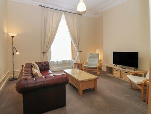 Ein Wohnzimmer mit einer Ledersofa, einem Holztisch, einem Fernseher und einer Lampe.