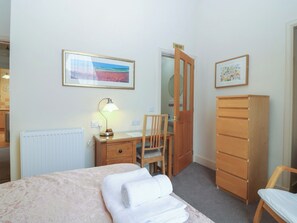 Ein Schlafzimmer mit einem Bett, einem Schreibtisch mit Lampe, einem Stuhl, einem Kleiderschrank und einer Tür zu einem weiteren Raum.