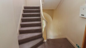 A carpeted staircase with white railings and a wall-mounted electrical box. - Pincerna Apartment Suite 1a (Aberdeen)